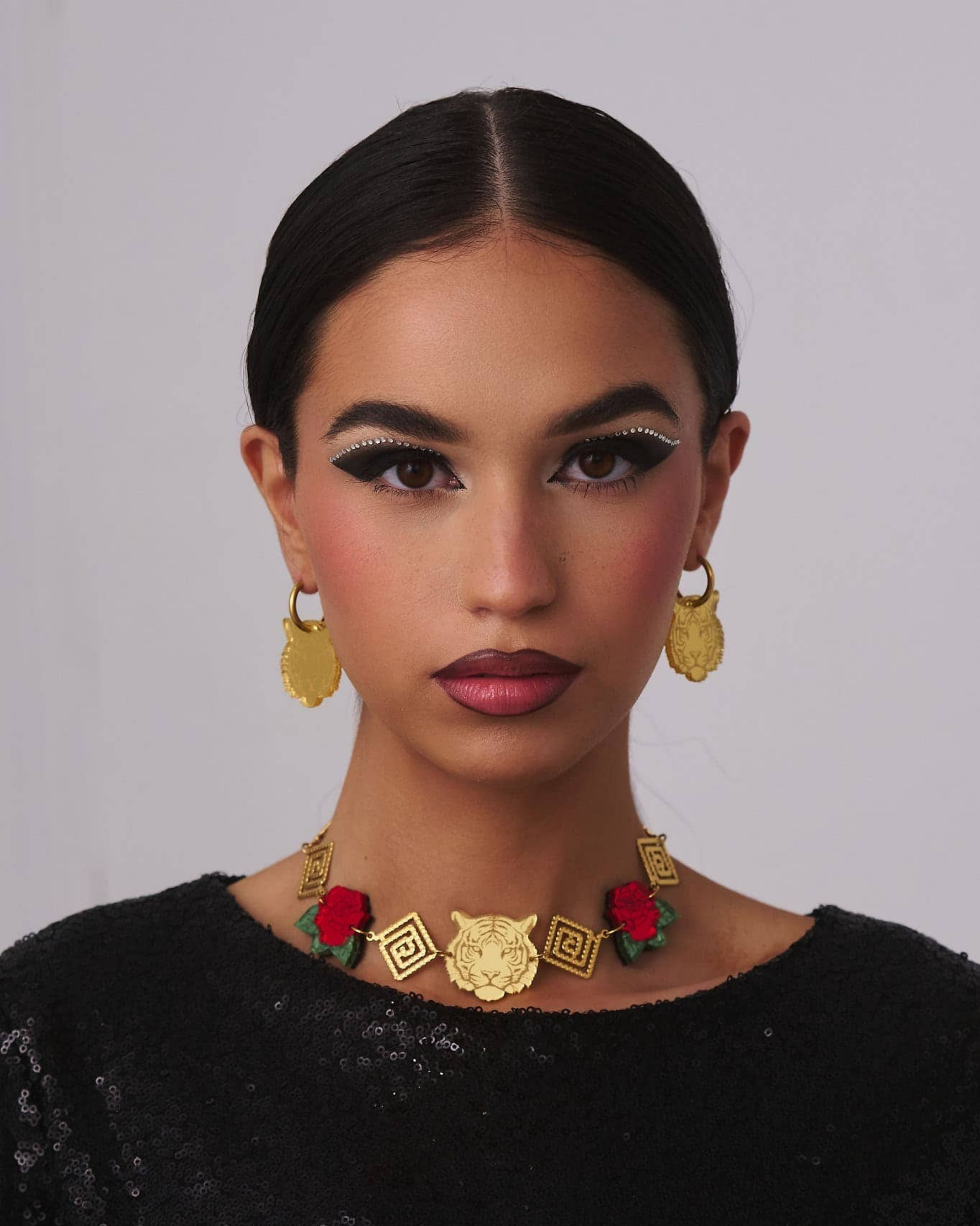 Person wearing gold tiger earrings with red flowers necklace against a gray background