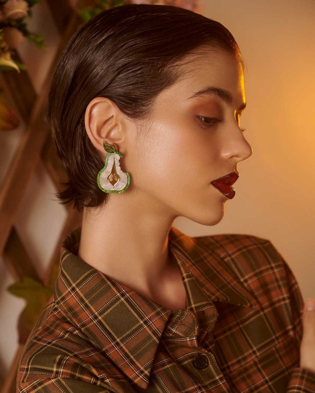 Person wearing pear shaped earrings and a plaid shirt with a blurred background