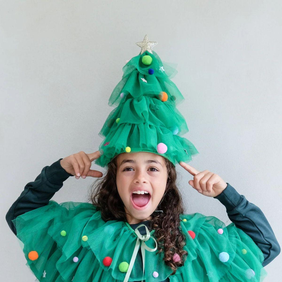 Child wearing a green Christmas tree costume with colorful decorations against a plain background