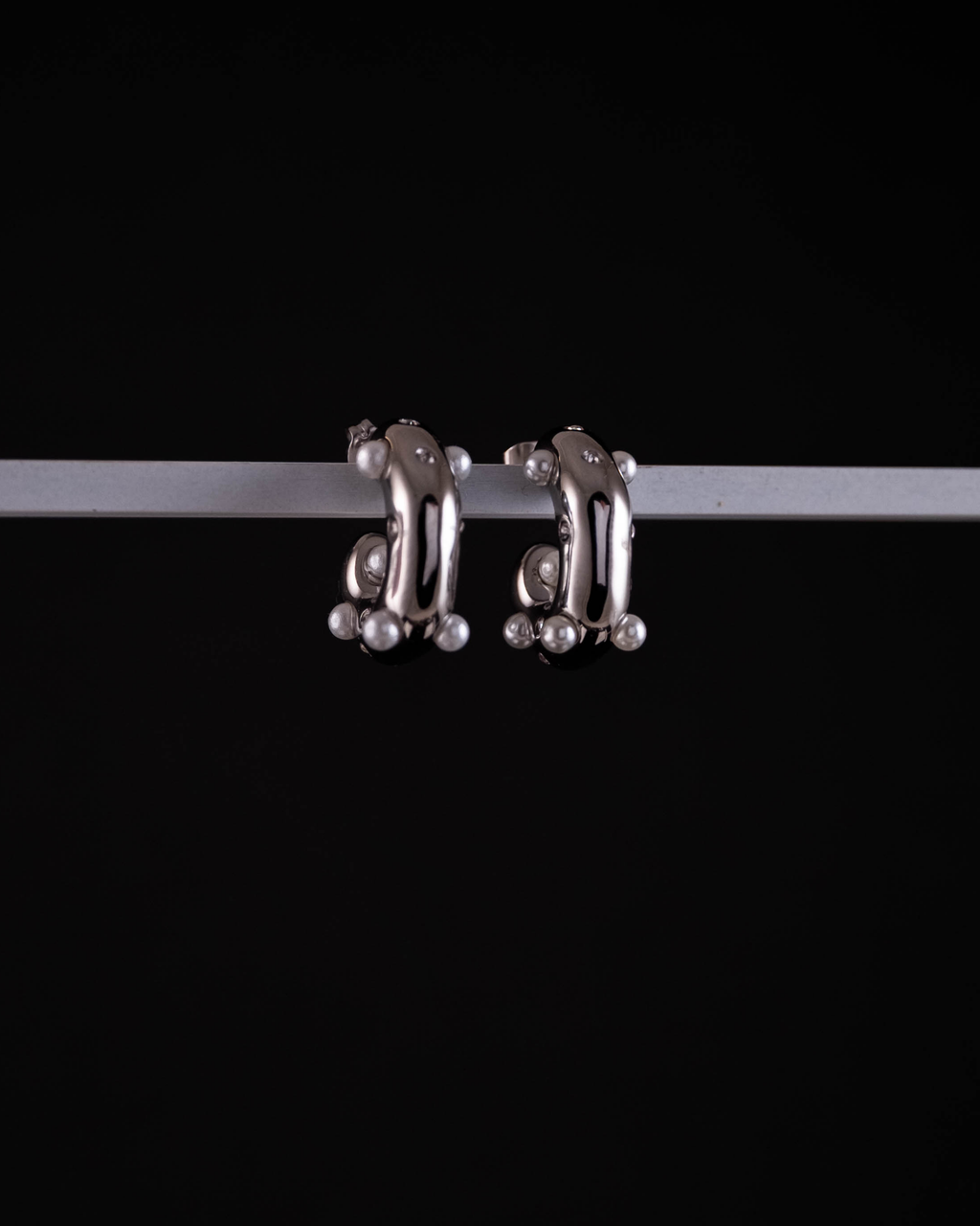 Pair of silver hoop earrings with small pearls on a black background