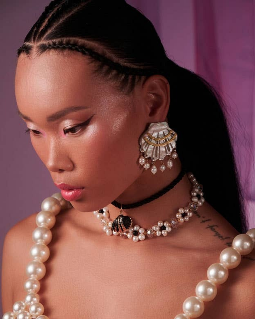 Person wearing shell earrings and pearl jewellery against a pink background