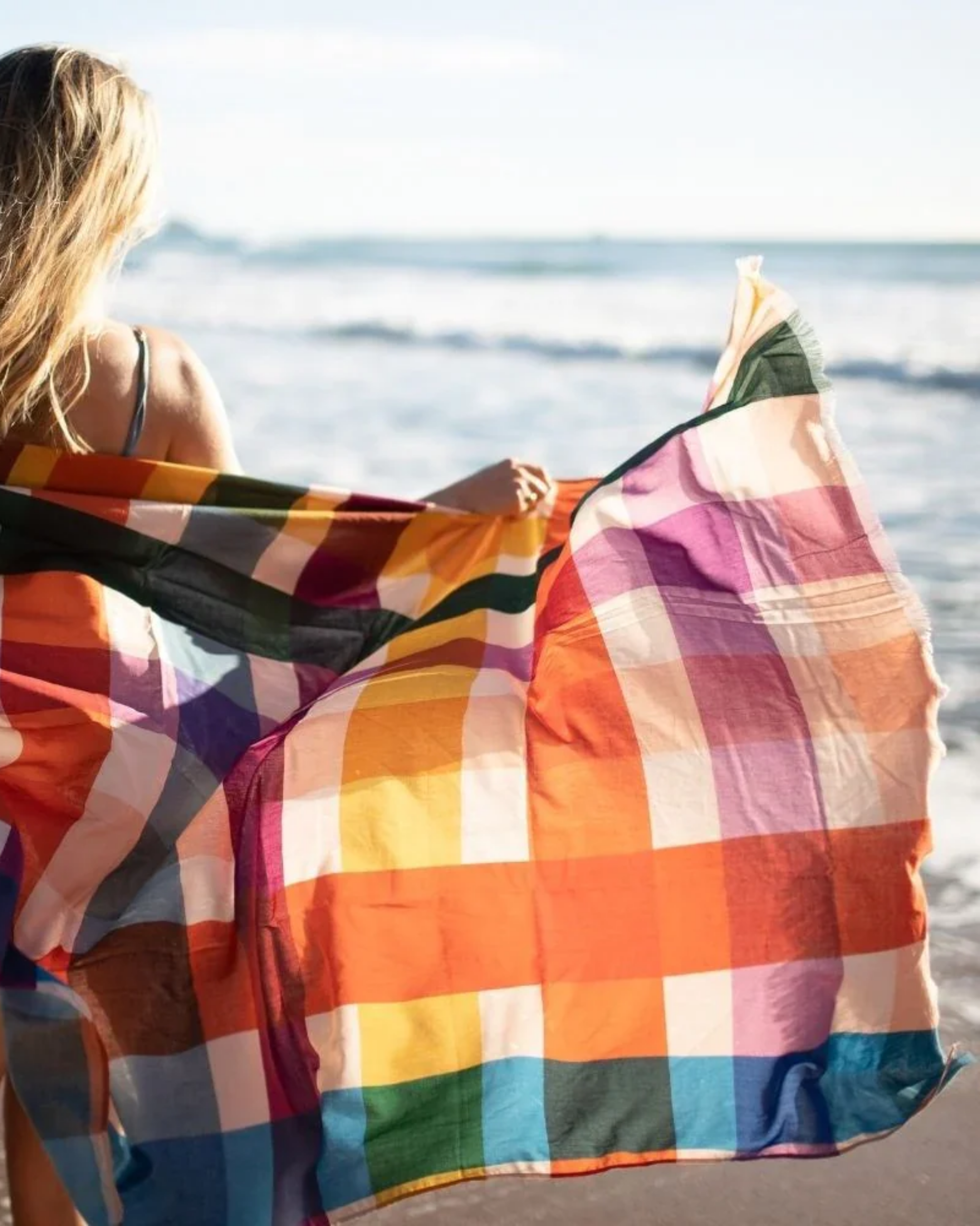 Person holding a colorful checkered towel by the ocean