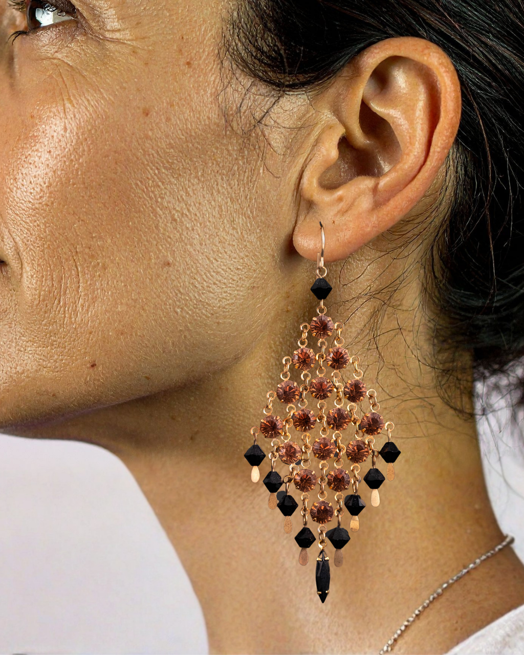 Close-up of a person wearing a chandelier earring with amber and black stones.