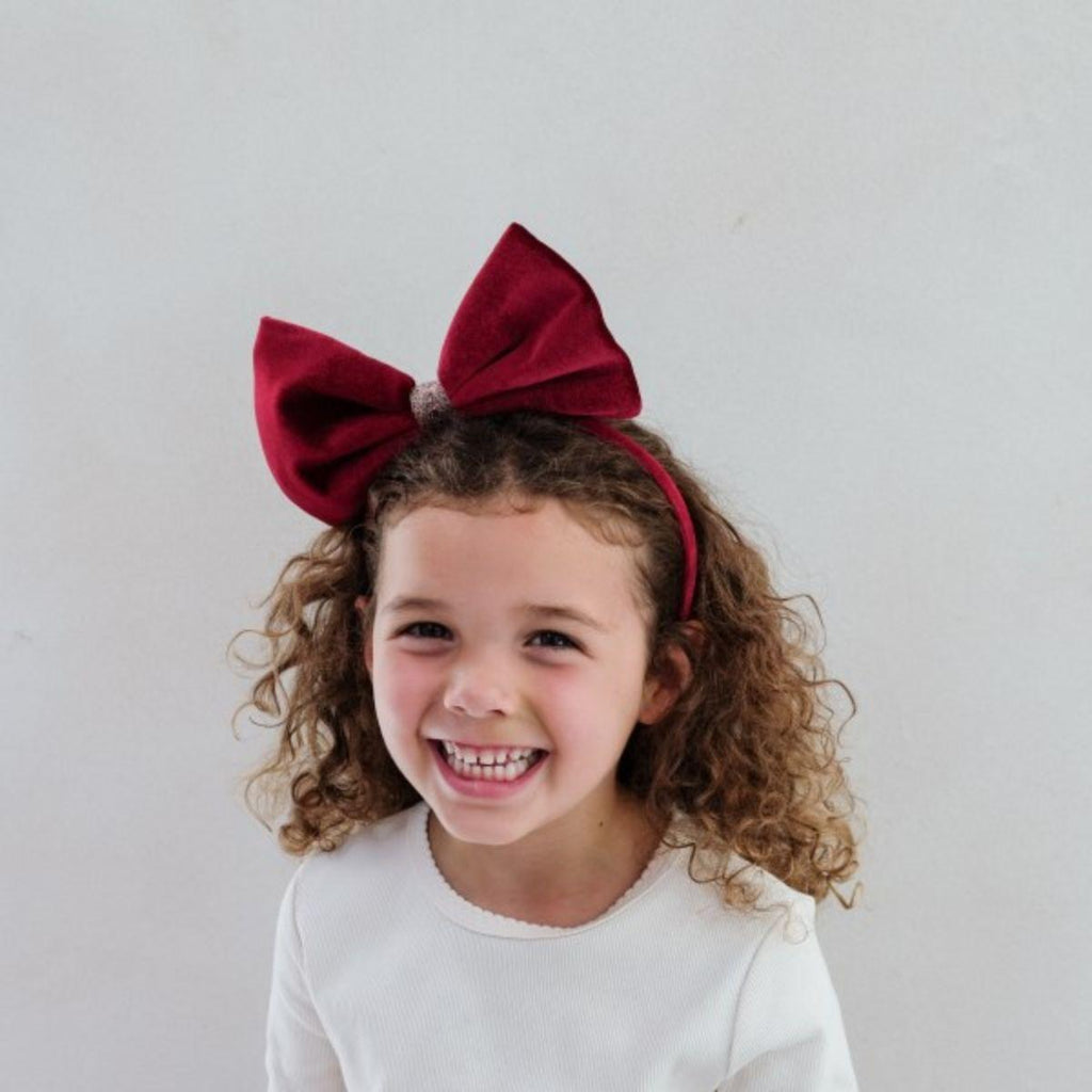 Child wearing a large red bow headband against a plain background