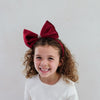 Child wearing a large red bow headband against a plain background