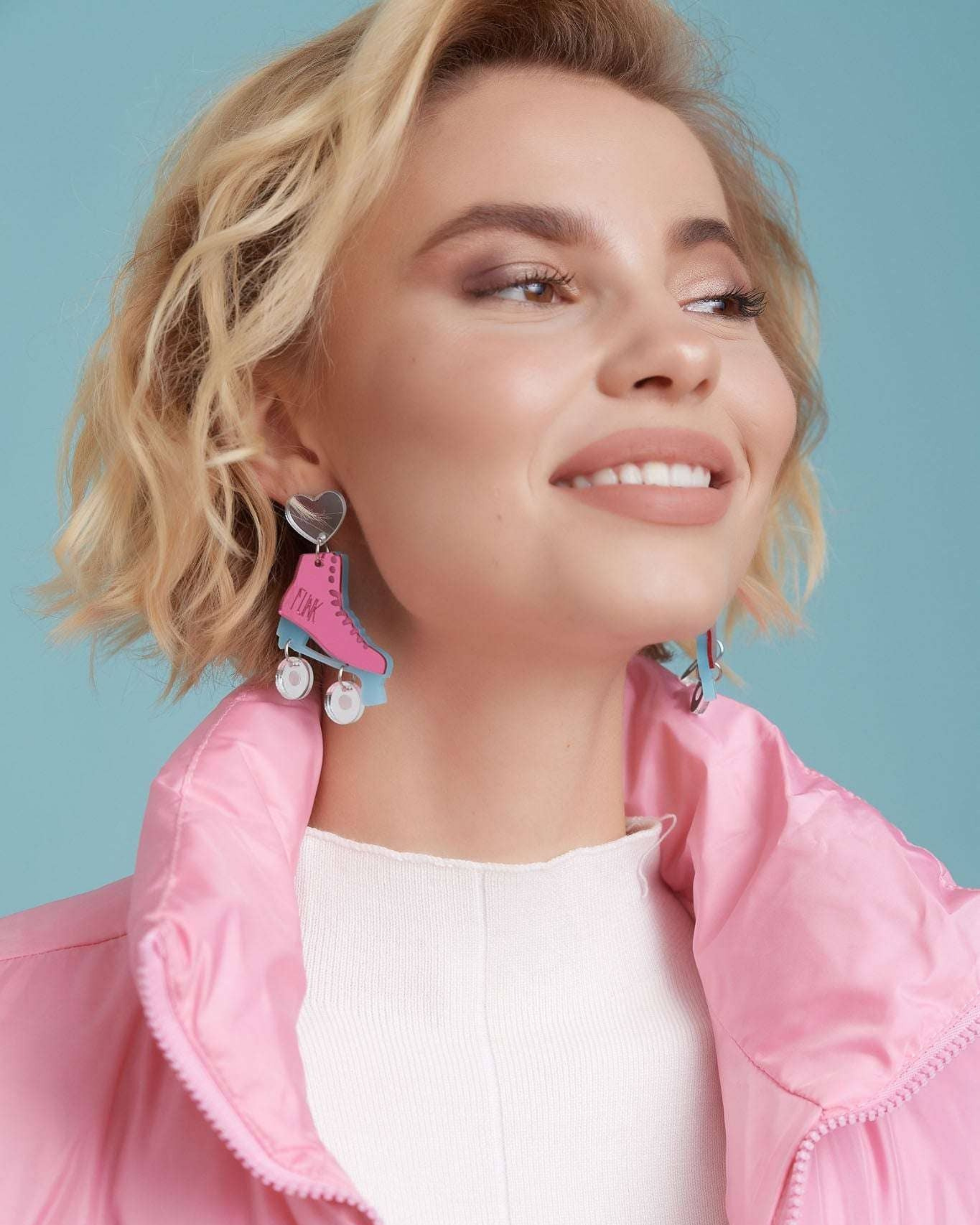 Woman wearing pink jacket and colorful earrings against a light blue background