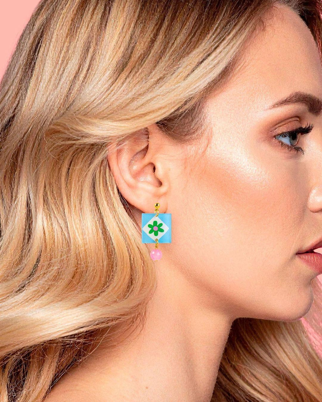 Close-up of a woman wearing colorful earrings with a pink background
