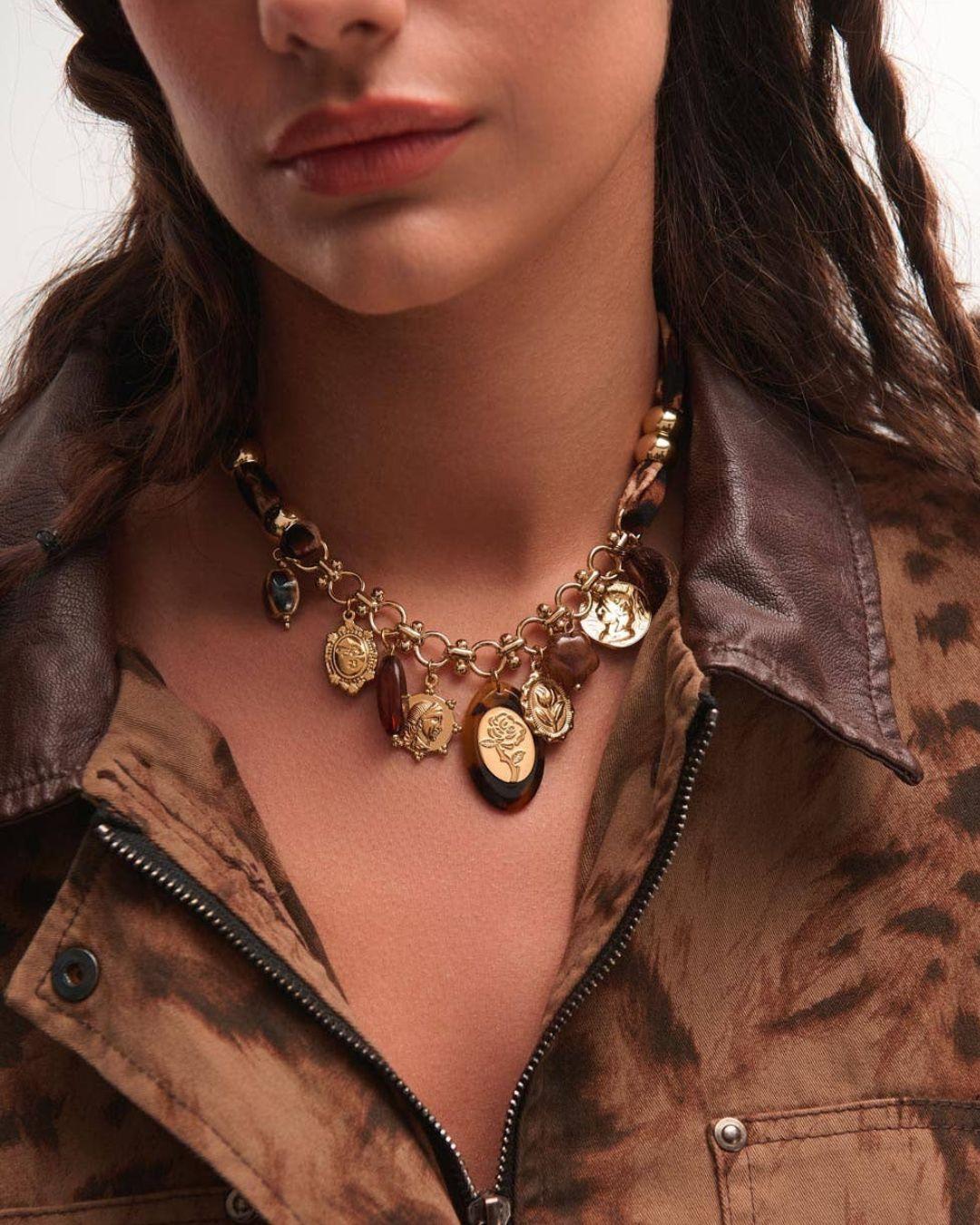 Close-up of a person wearing a gold necklace with various pendants against a neutral background.