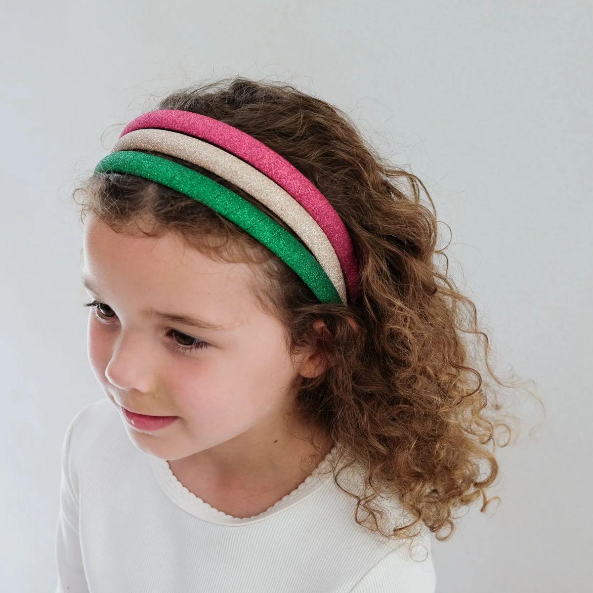 Female presenting child wearing a colorful headband against a plain background