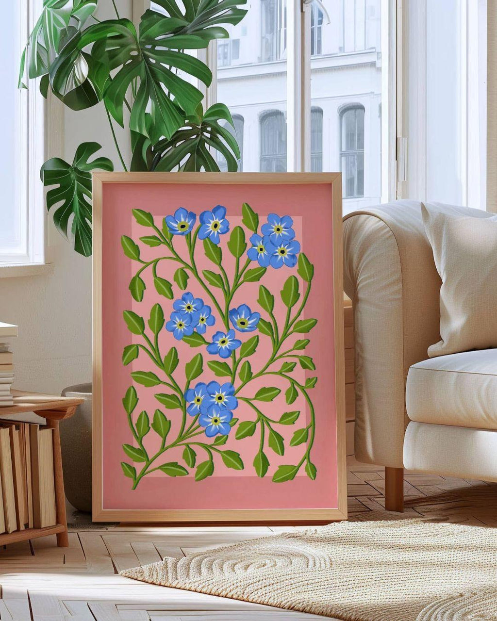 Framed floral artwork with blue flowers and green leaves on a pink background, placed in a living room.