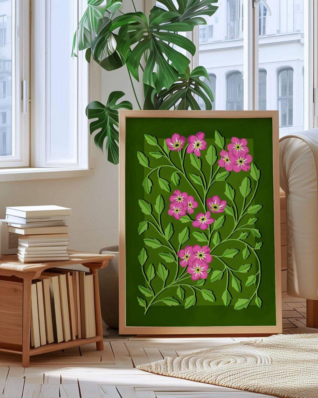 Framed floral artwork with pink flowers and green leaves on a green background, placed in a room with a window and books.