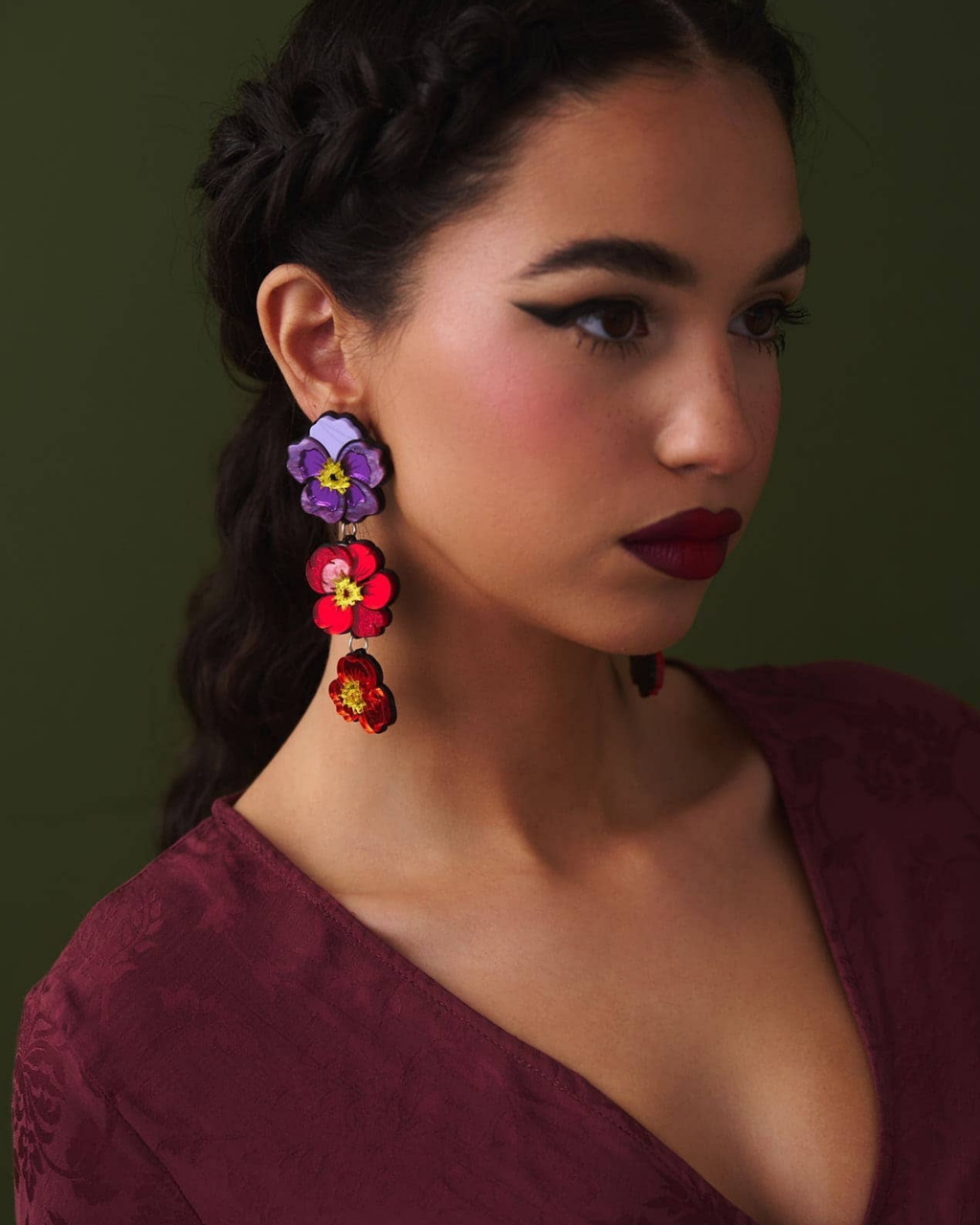 Woman wearing colorful floral earrings against a dark background