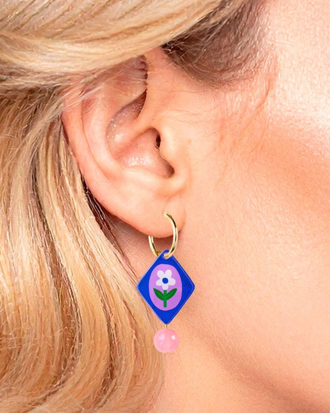Close-up of an ear wearing a colorful earring with a flower design.