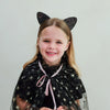 Child wearing a black star-patterned cape and cat ears against a plain background