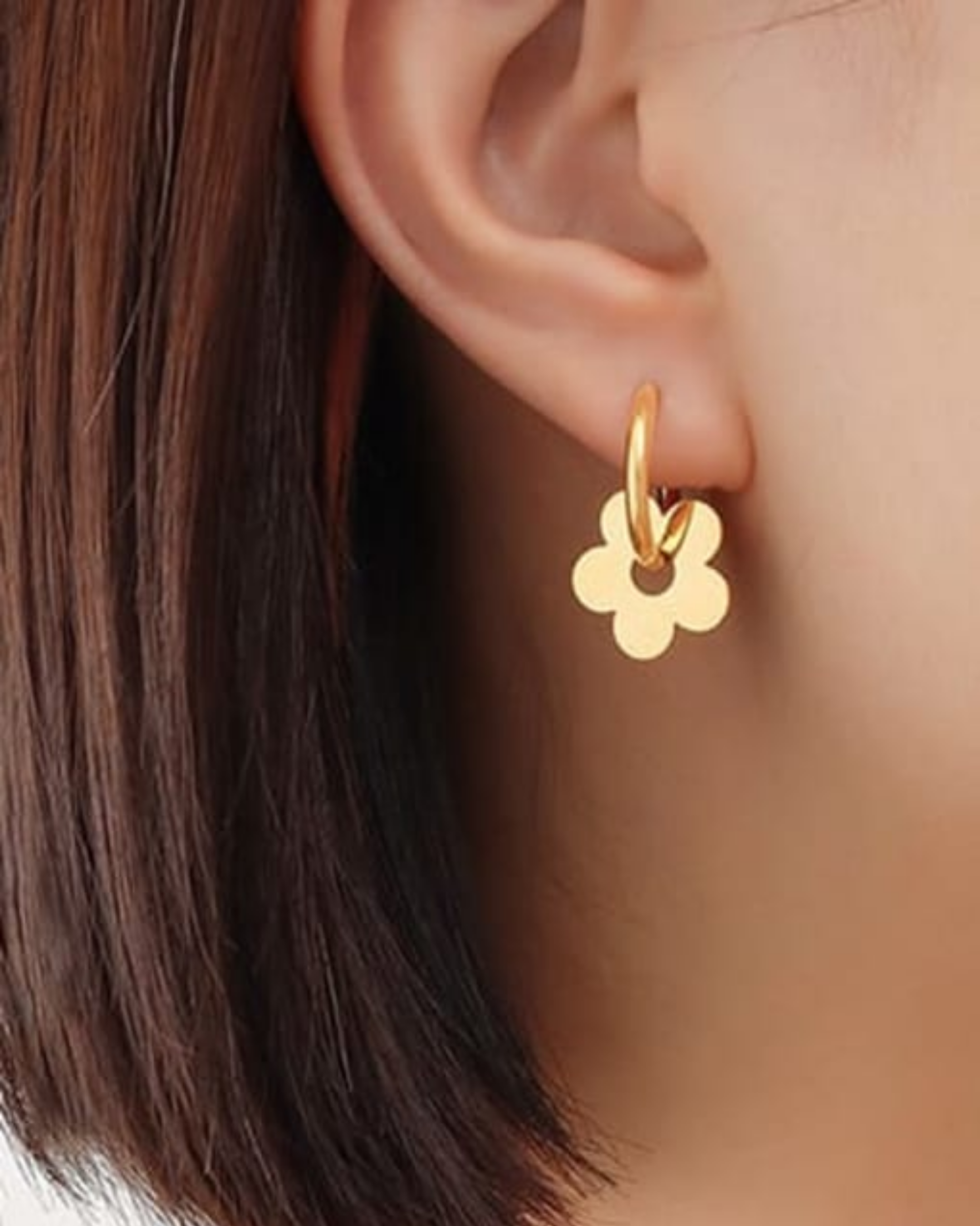 Gold flower-shaped earring worn by a person with brown hair.