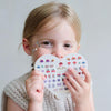 Child holding a heart-shaped sheet of stickers with various designs on a plain background