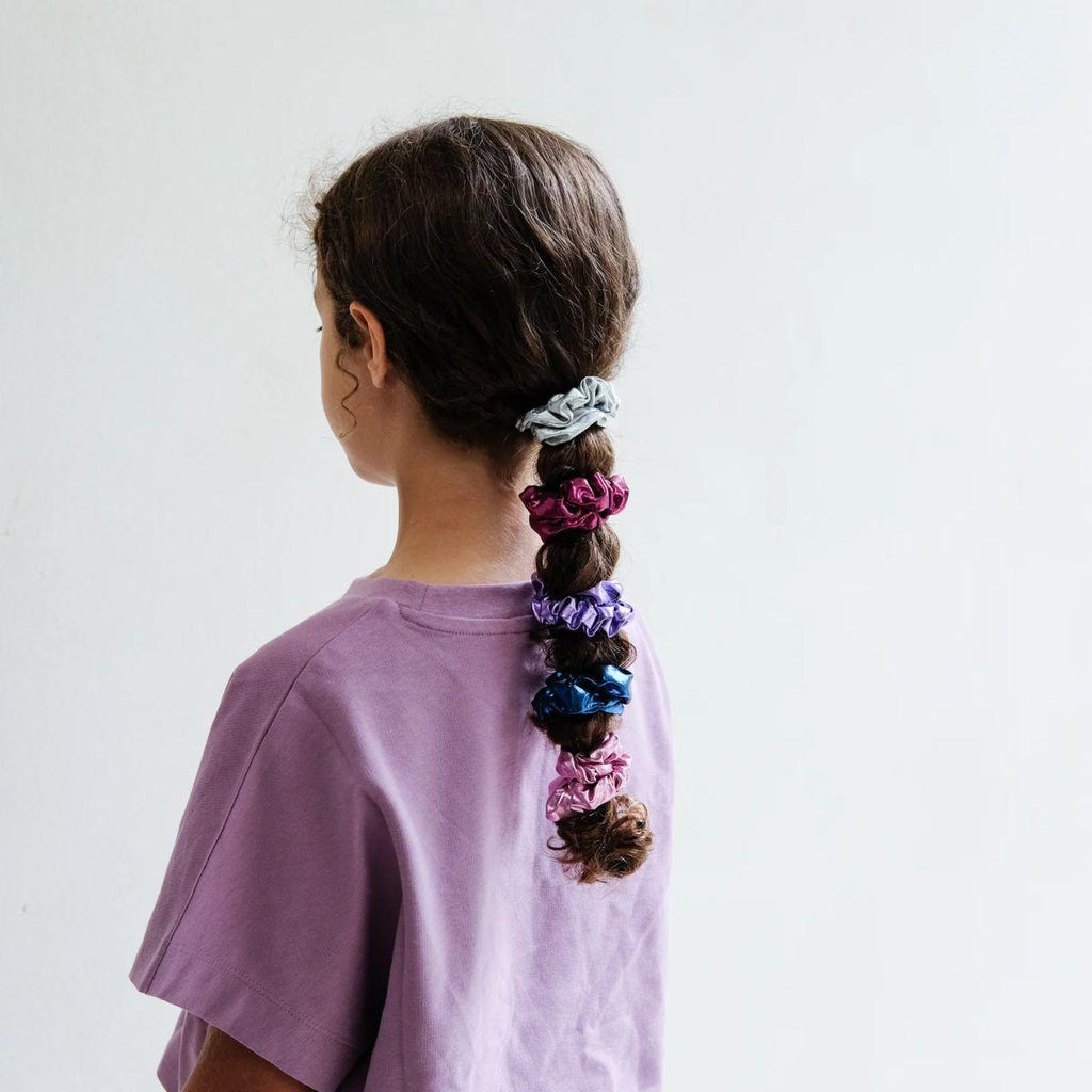Person with colorful hair ties in a braid on a plain background