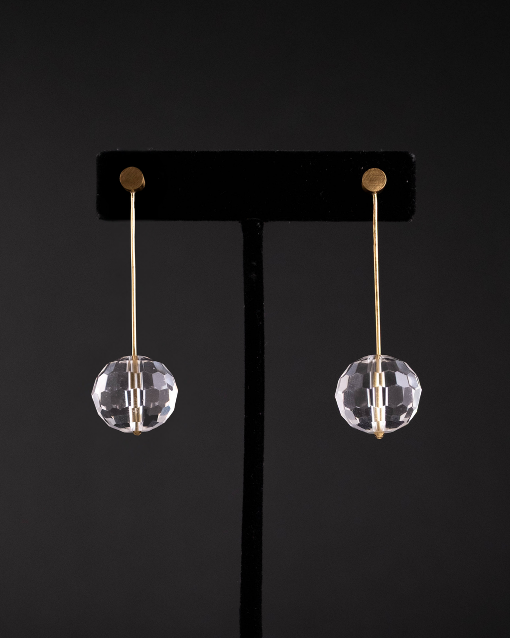 Pair of crystal earrings on a black stand against a black background