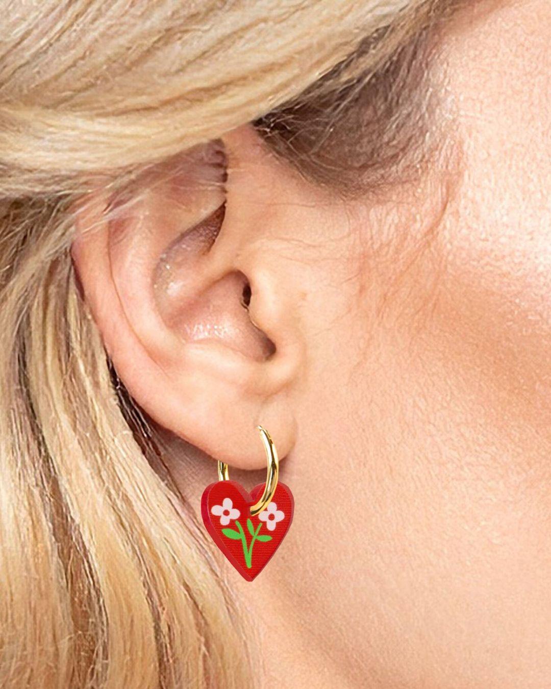 Red heart-shaped earring with floral design worn by a person with blonde hair.