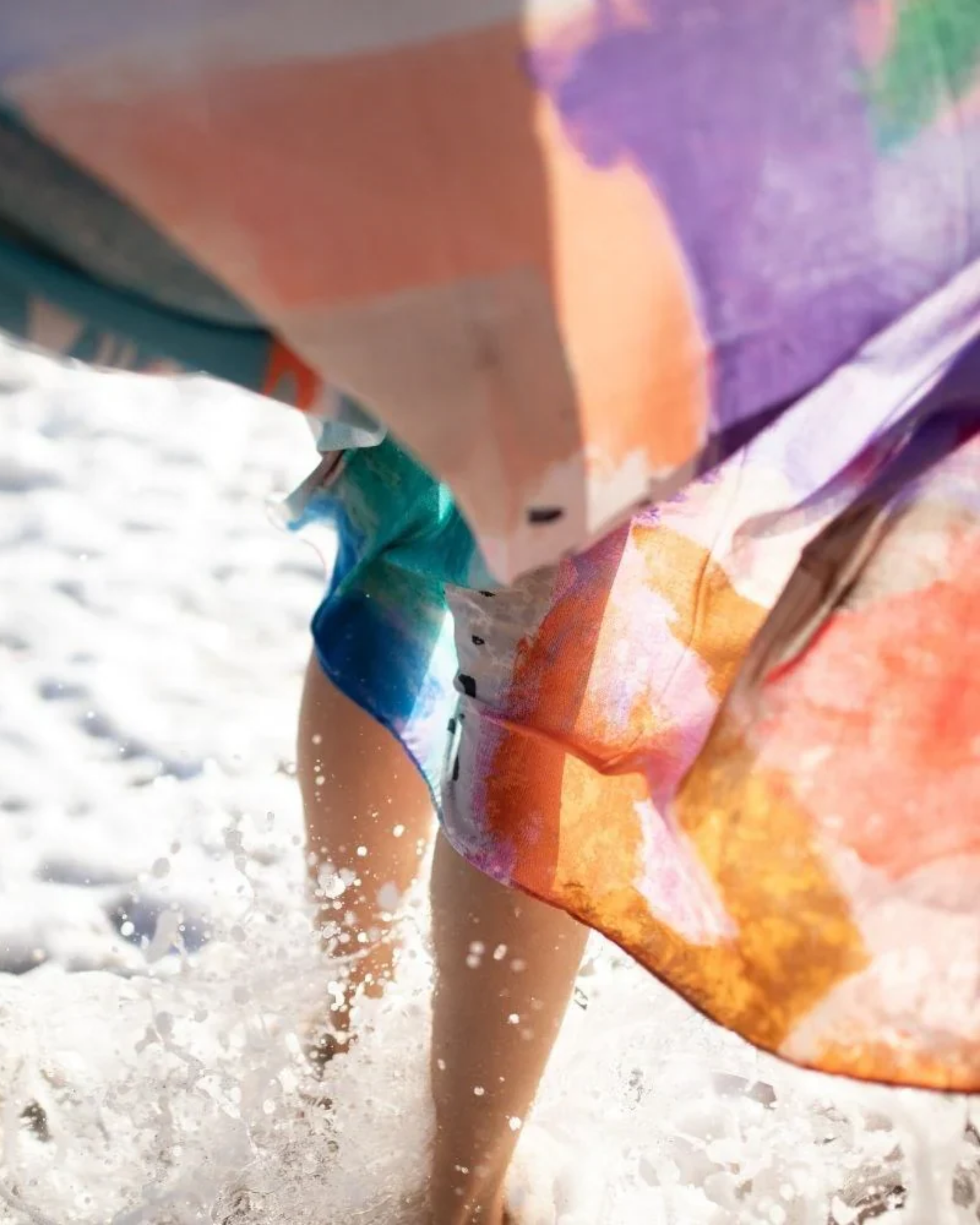 Person holding a colorful sarong with water splashing around, likely at a beach.