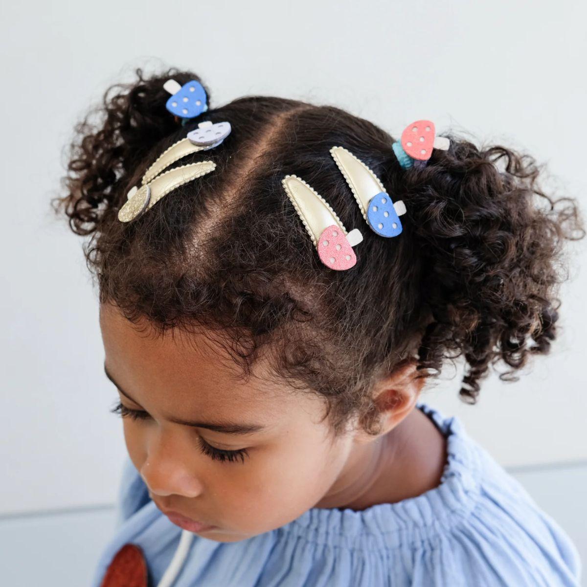 Child with curly hair wearing colorful hair clips against a light background