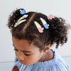 Child with curly hair wearing colorful hair clips against a light background