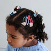 Child with braided hair adorned with colorful hair clips against a light background