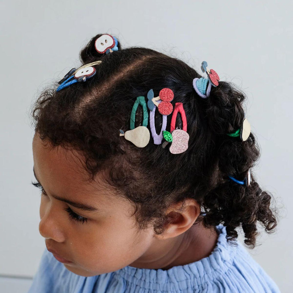 Child with braided hair adorned with colorful hair clips against a light background
