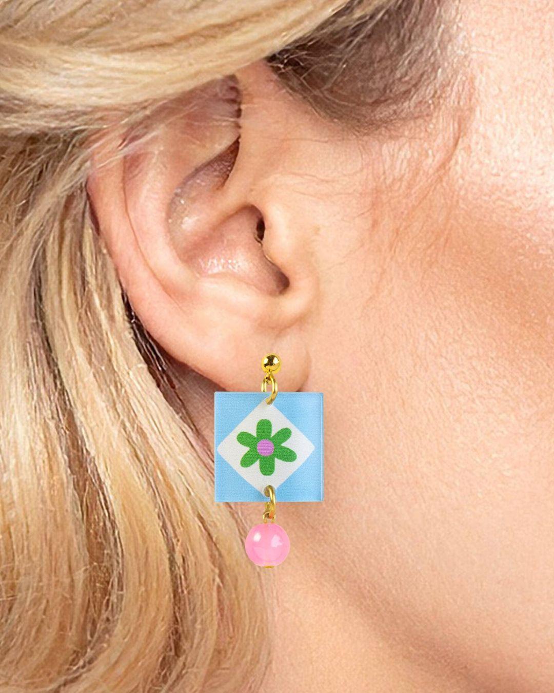 Close-up of an ear wearing a colorful earring with a flower design.