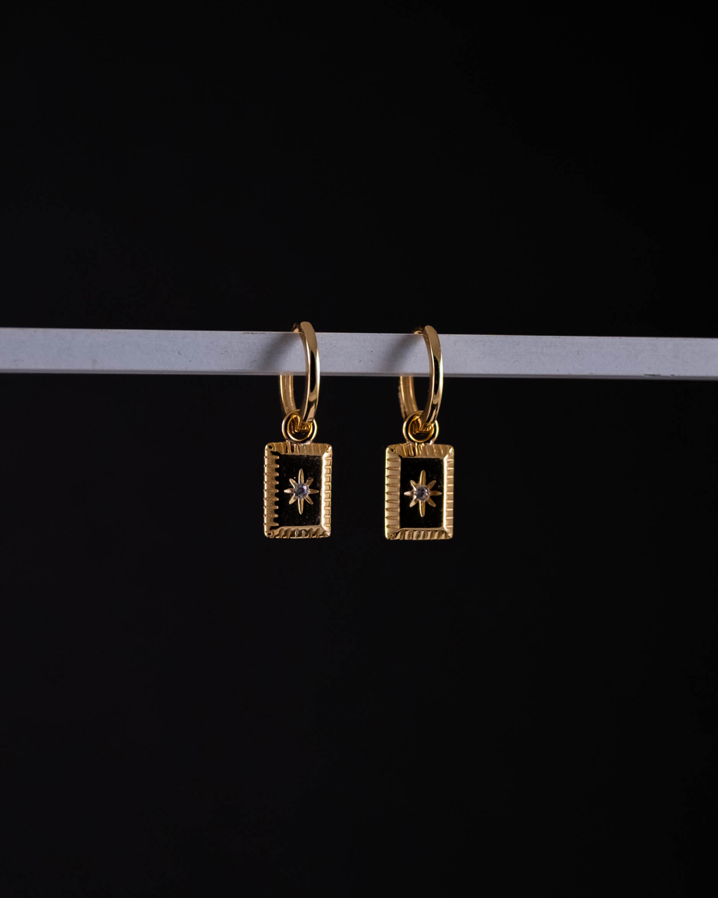 Gold hoop earrings with star designs on a black background