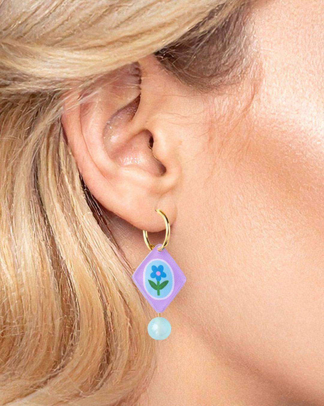 Close-up of an ear wearing a purple hoop earring with floral design