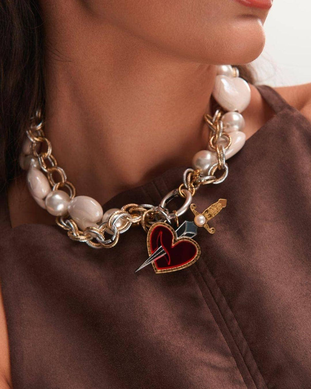 Person wearing a necklace with heart and sword charms against a plain background