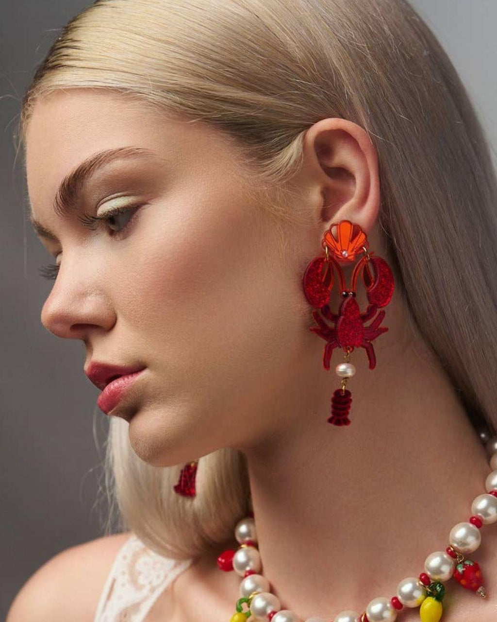 Close-up of a person wearing lobster earrings with a grey background
