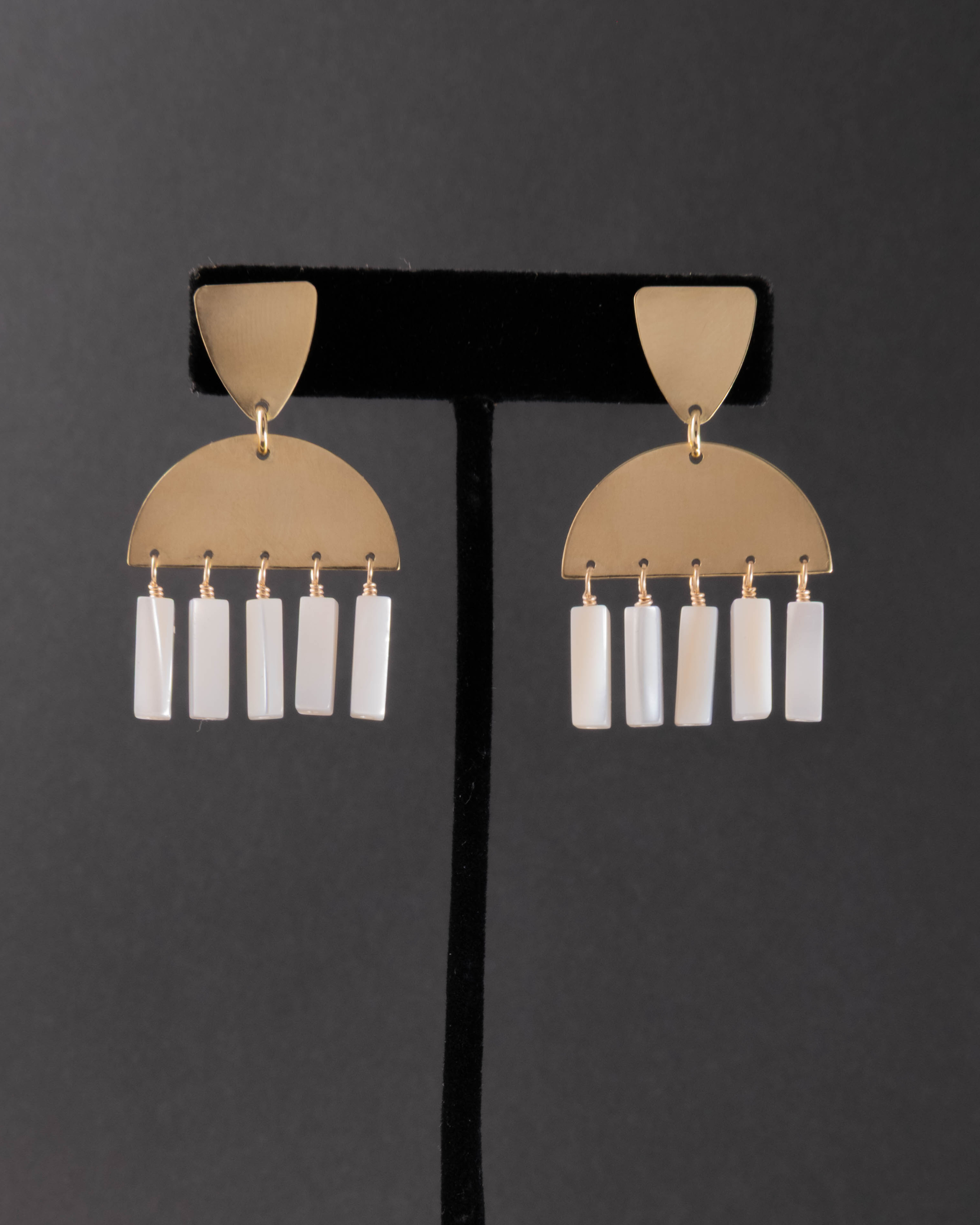 Pair of gold and mother of pearl earrings on a black stand against a dark background