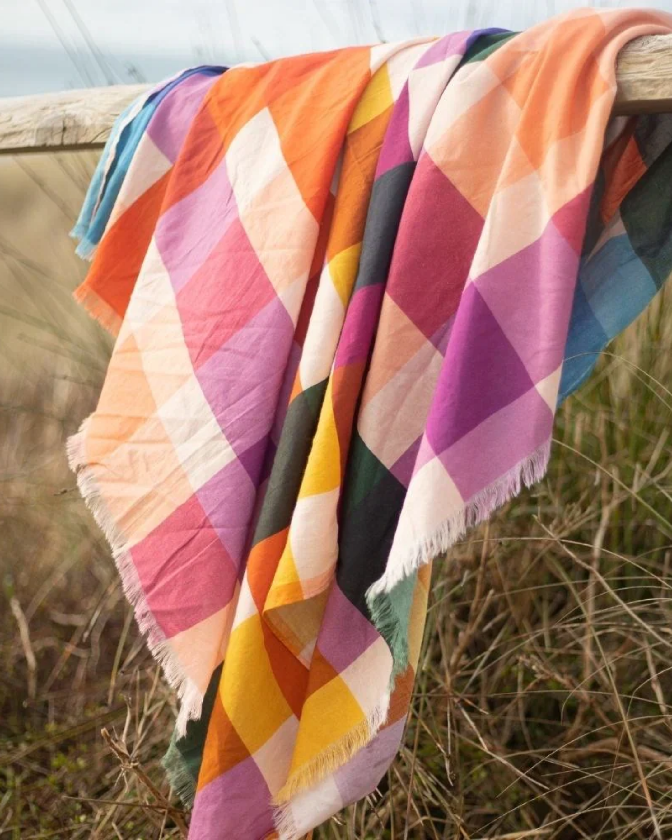 Colorful checkered sarong draped over a wooden railing in a natural setting.