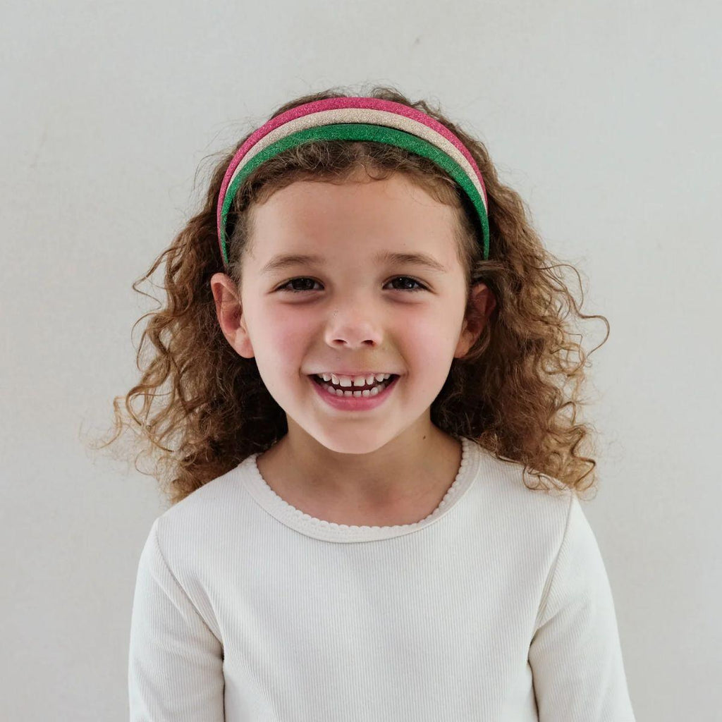 Female presenting child with a colorful headband smiling against a plain background