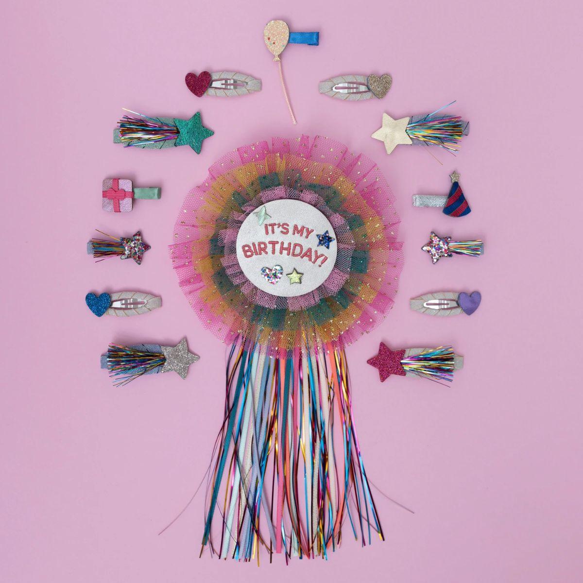 Birthday rosette with colorful tassels and hair accessories on a pink background