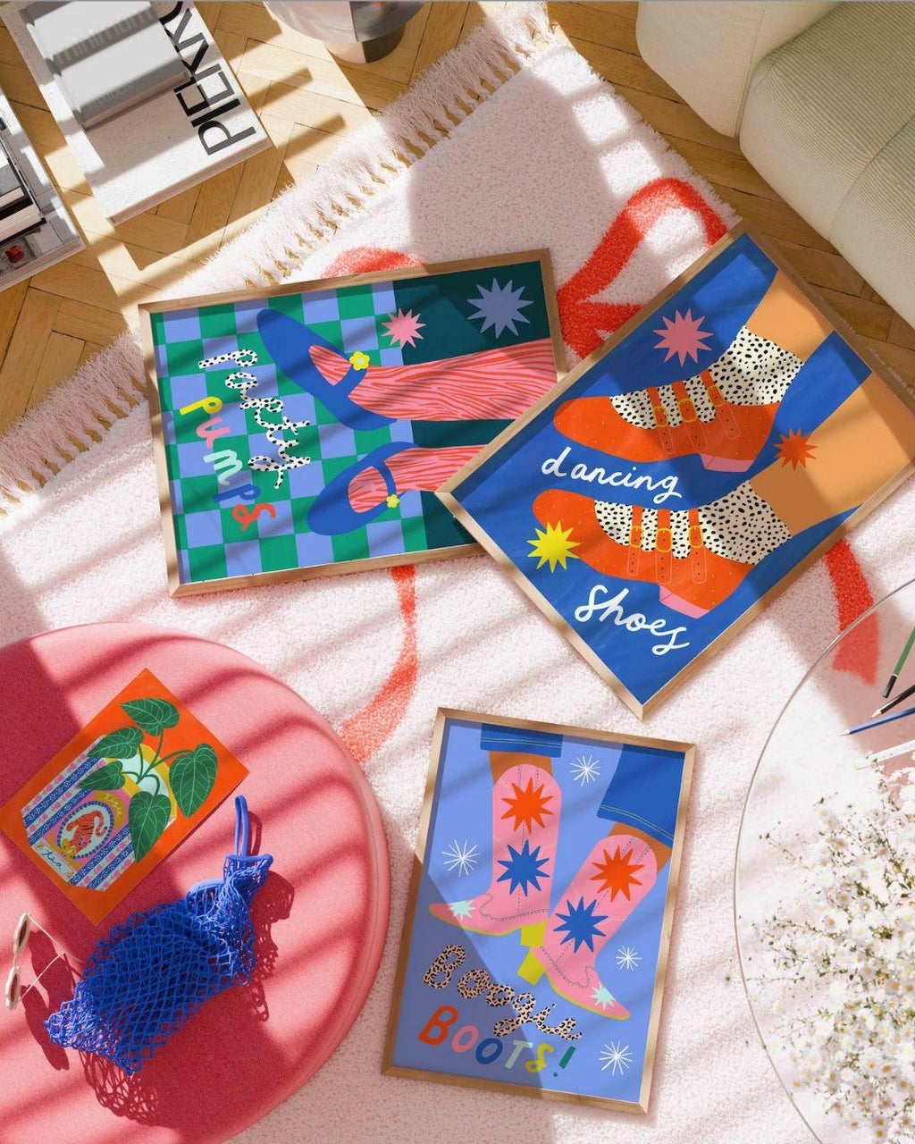 Colorful abstract art prints on a table with a pink surface and white flowers.