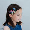 Girl with colorful dinosaur hair clips in her hair against a plain background