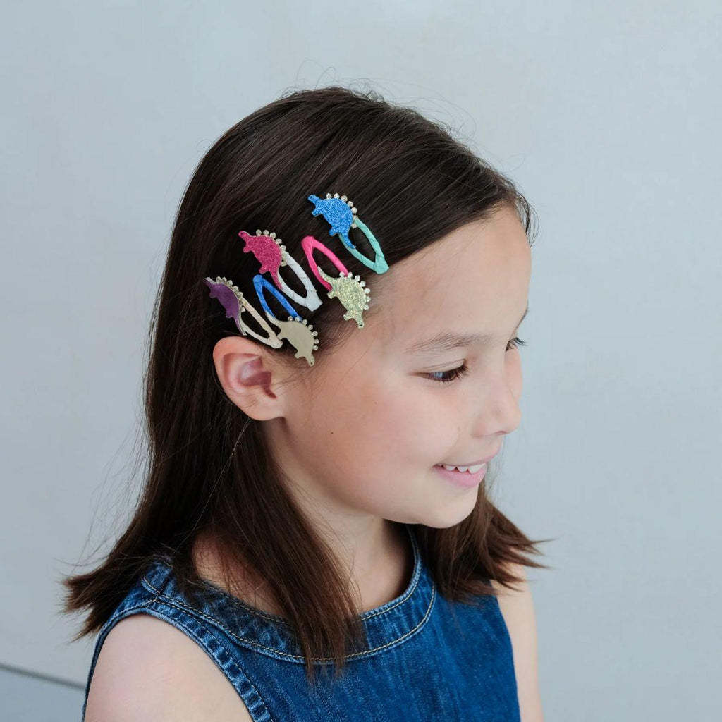 Girl with colorful dinosaur hair clips in her hair against a plain background