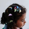 Child with colorful dinosaur hair clips in braided hair against a plain background