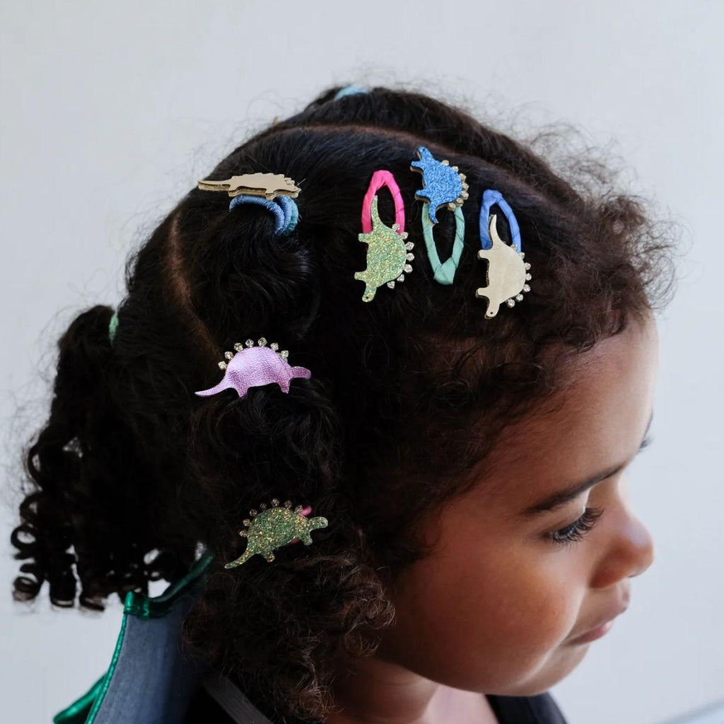 Child with colorful dinosaur hair clips in braided hair against a plain background