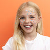 Young girl with colorful stickers on her face against an orange background