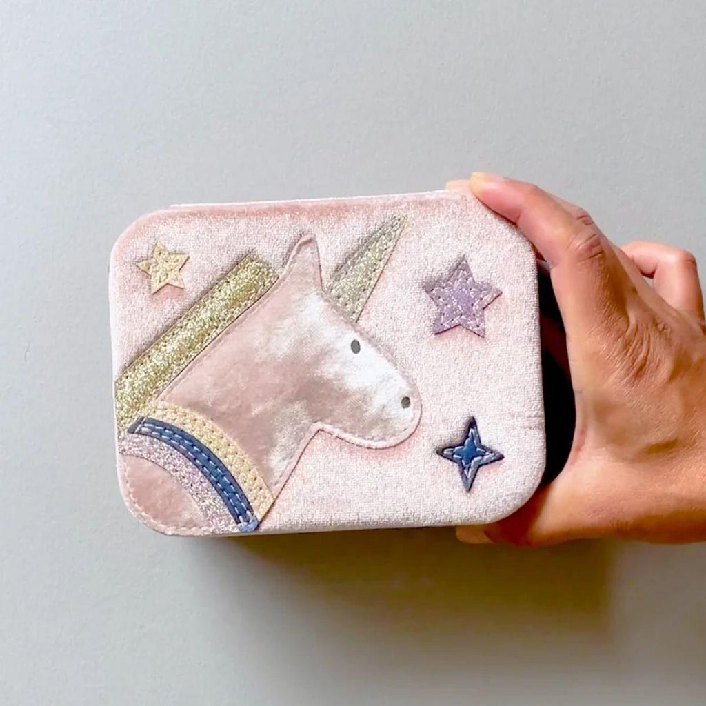 Hand holding a pink pouch with unicorn and star designs on a light gray background