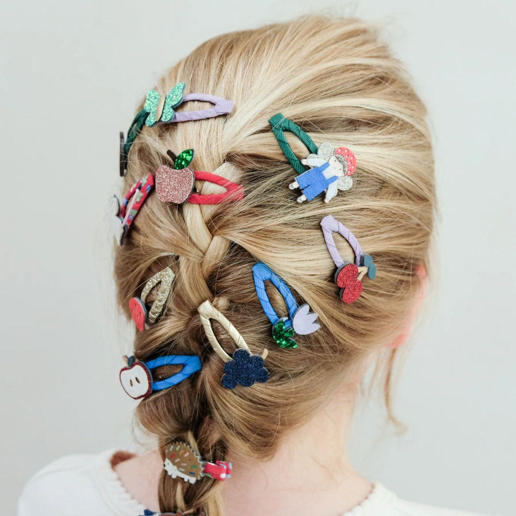 Person with braided hair adorned with colorful hair clips on a plain background