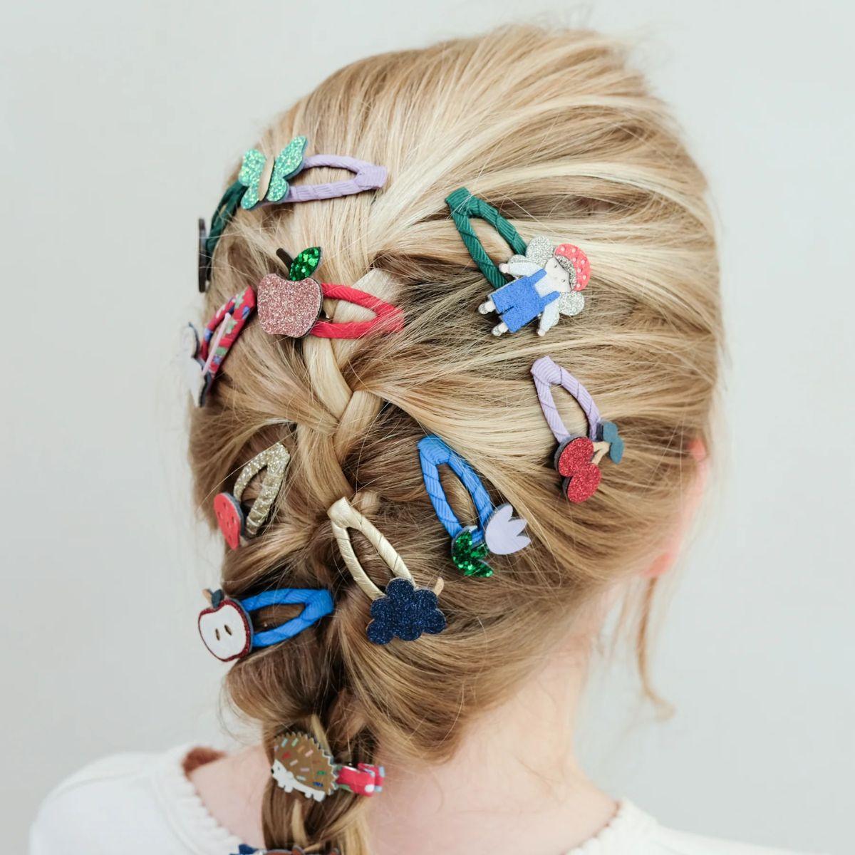 Person with braided hair adorned with colorful hair clips on a plain background