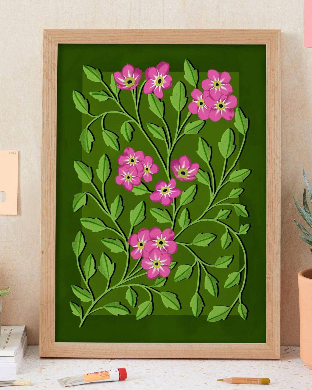 Framed artwork with pink flowers and green leaves on a green background