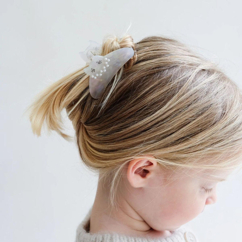Child with blonde hair tied up wearing a decorative hair clip on a light background