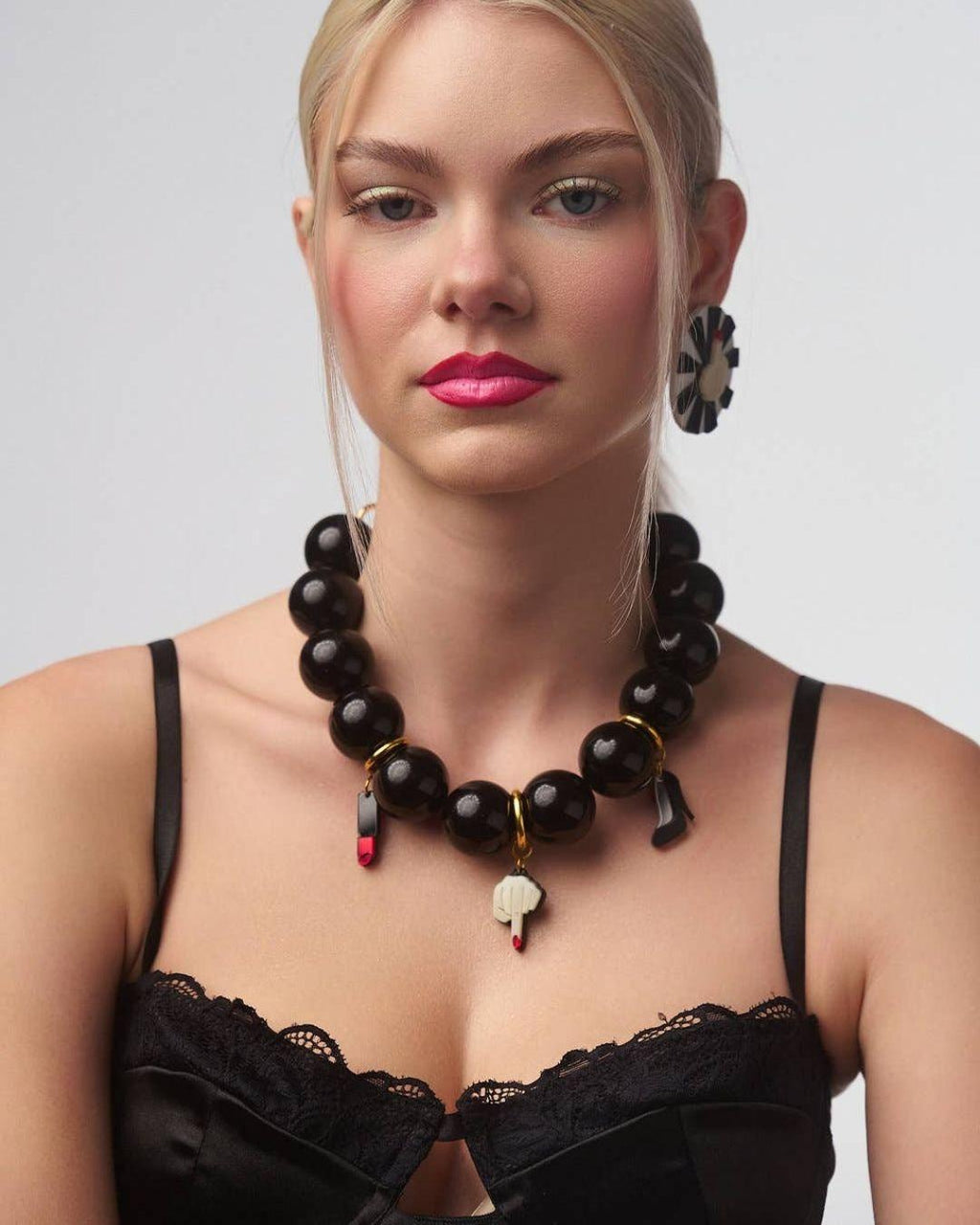 Person wearing Statement barbie Black beaded necklace with gold chain and various charms on a white background 