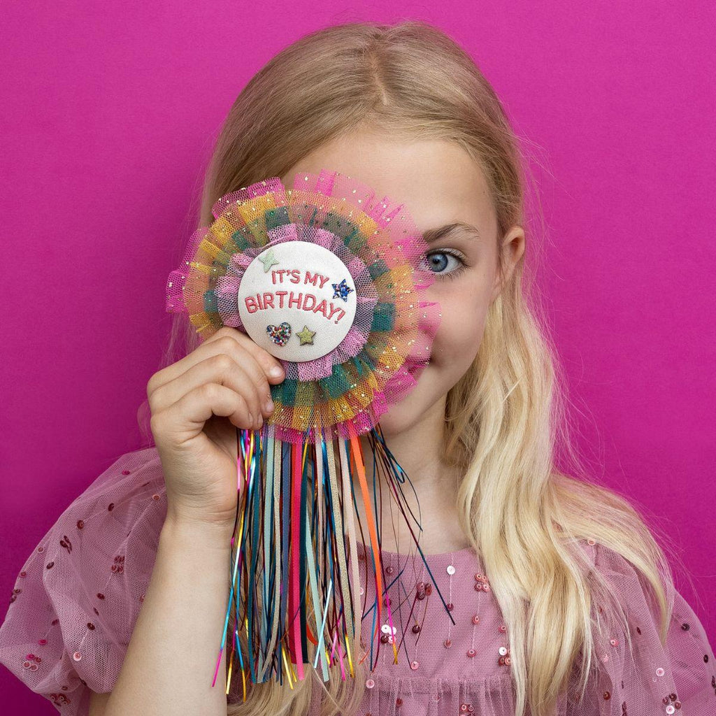 Young girl holding a colorful birthday party hat against a pink background